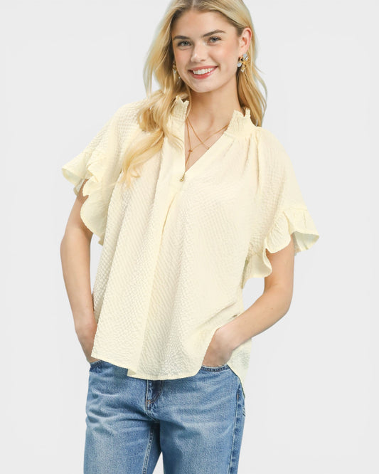 Woman wearing a light yellow blouse with ruffled sleeves and blue jeans on a white background