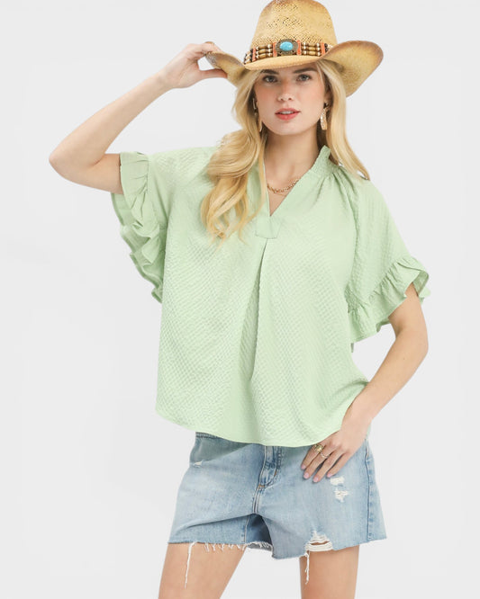 Woman wearing a light green blouse and denim shorts with a straw hat on a white background