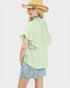 Young girl wearing a light green blouse with ruffled sleeves and denim shorts on a white background