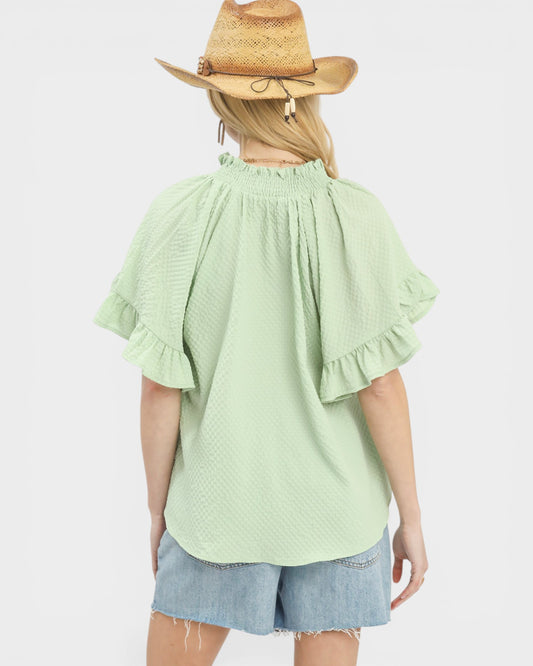 Person wearing a light green blouse with ruffled sleeves and denim shorts on a white background