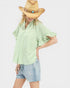 Woman wearing a light green blouse, denim shorts, and a straw hat with beads on a white background