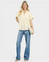 Woman wearing a light yellow blouse and blue jeans on a white background