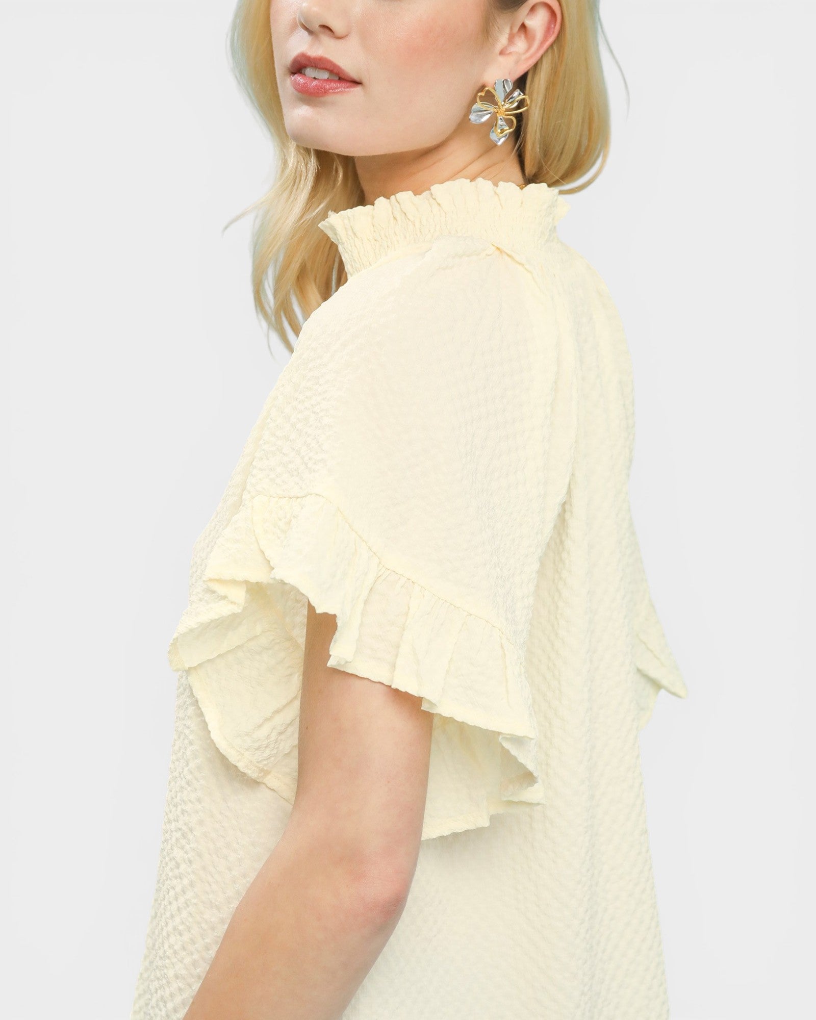 Woman wearing a light yellow ruffled blouse on a white background