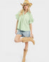 Woman wearing a light green blouse, denim shorts, and tan boots on a white background