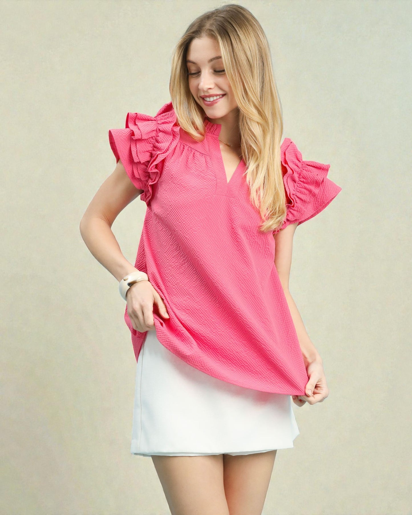 Woman wearing a pink blouse with ruffled sleeves on a beige background