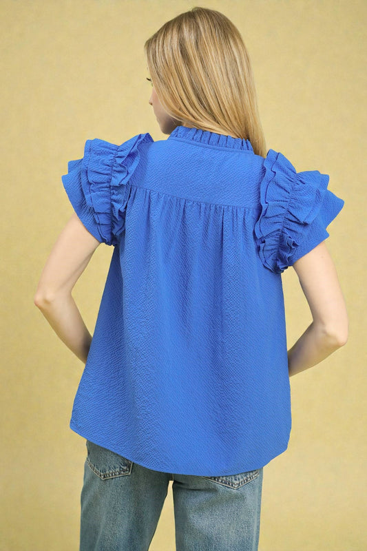 Woman wearing a blue blouse with ruffled sleeves against a beige background