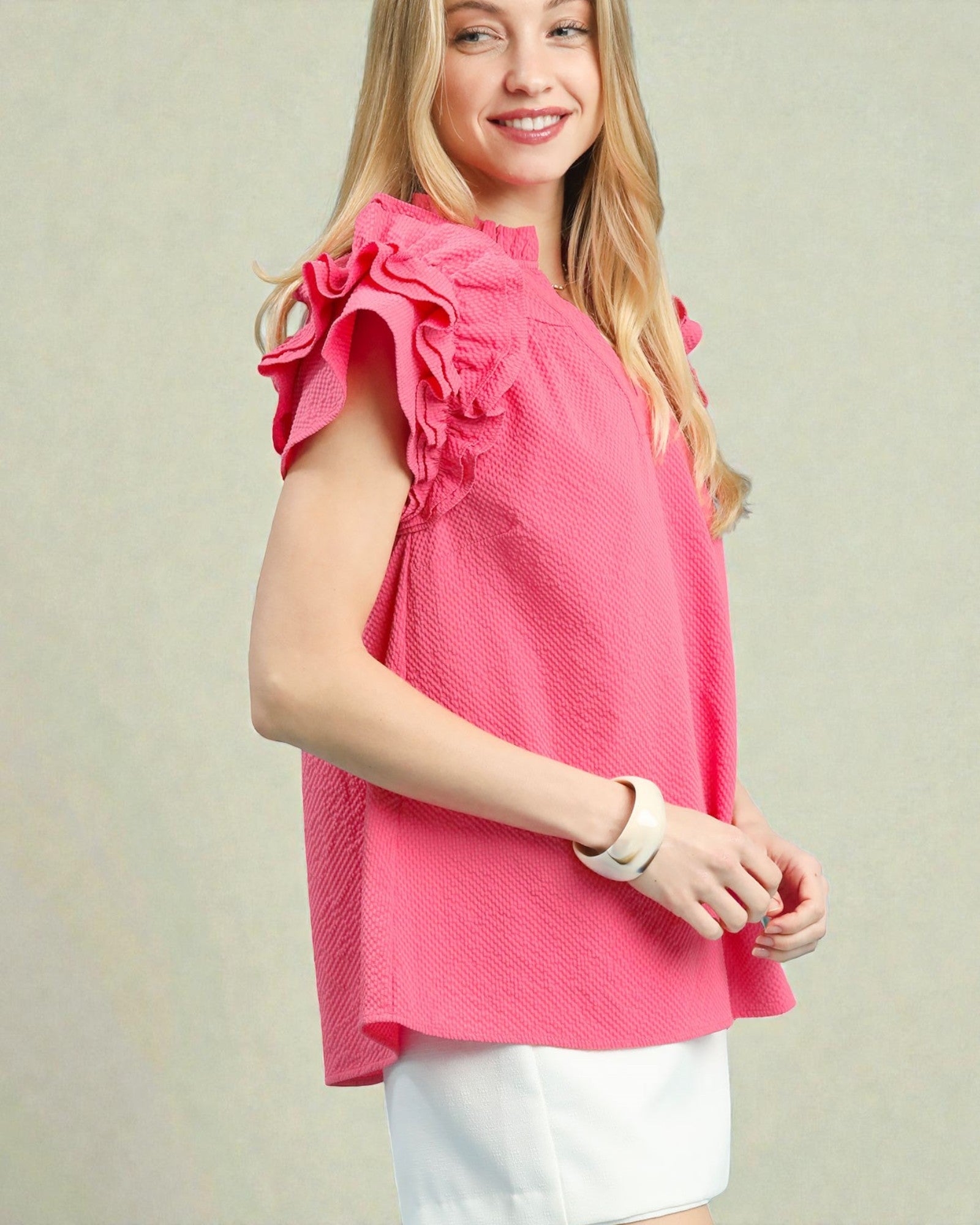 Woman wearing a pink blouse with ruffled shoulders against a plain background