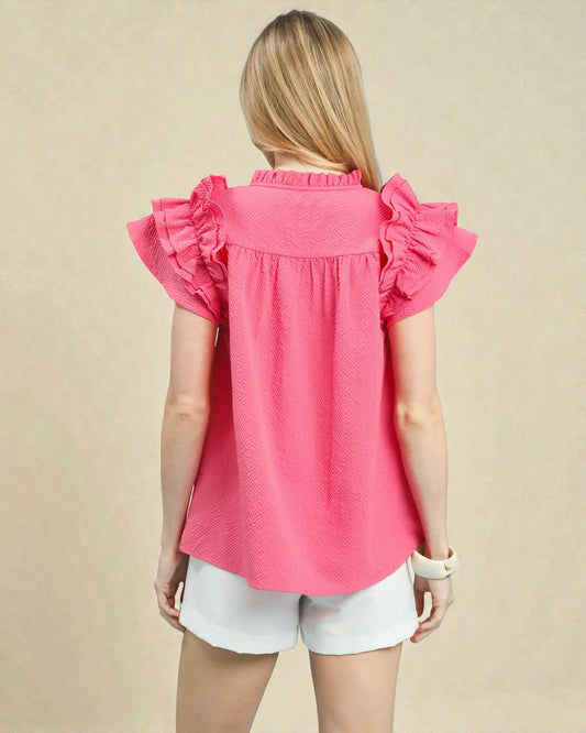 Person wearing a pink blouse with ruffled sleeves on a beige background