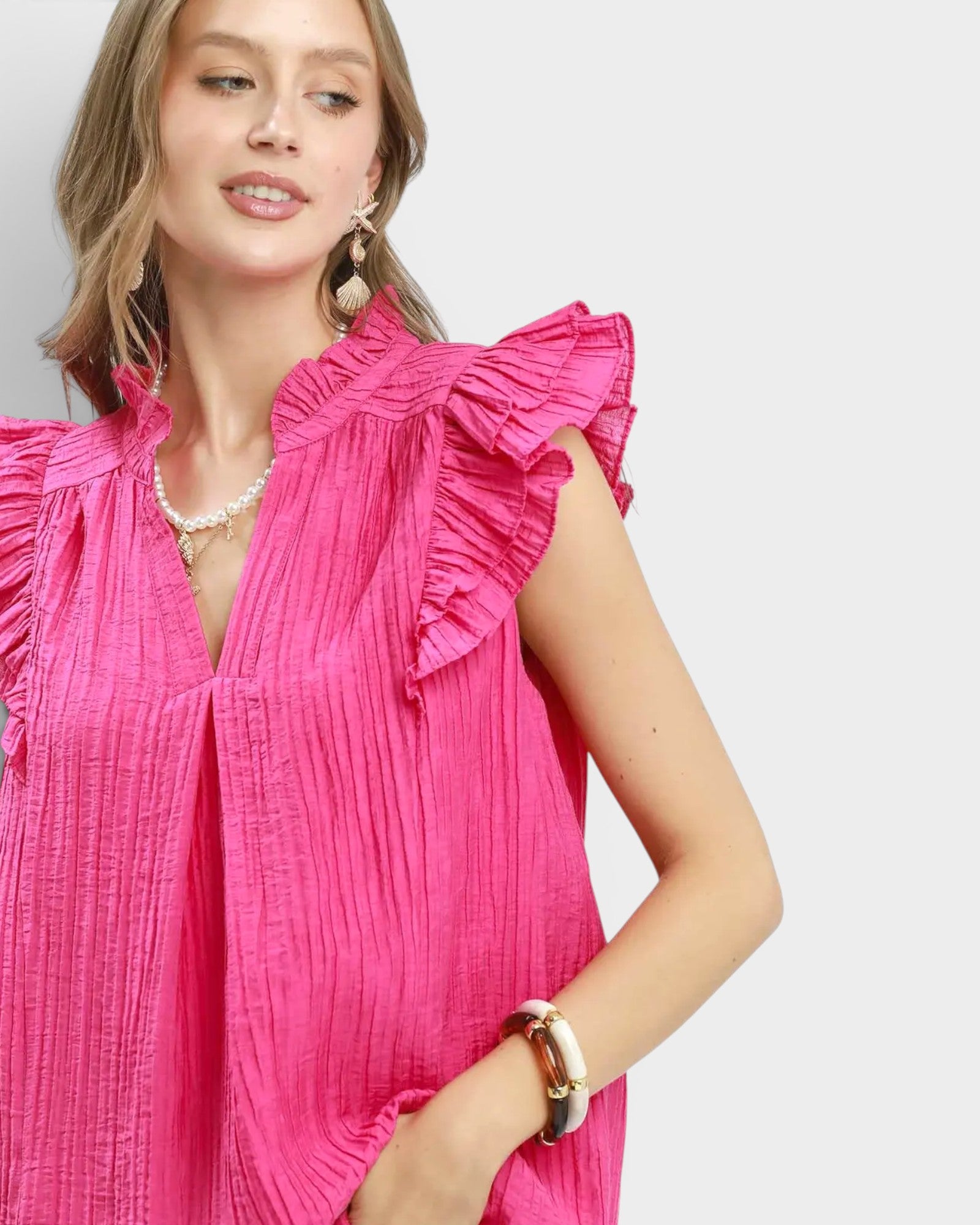 Woman wearing a bright pink dress with ruffled sleeves on a white background