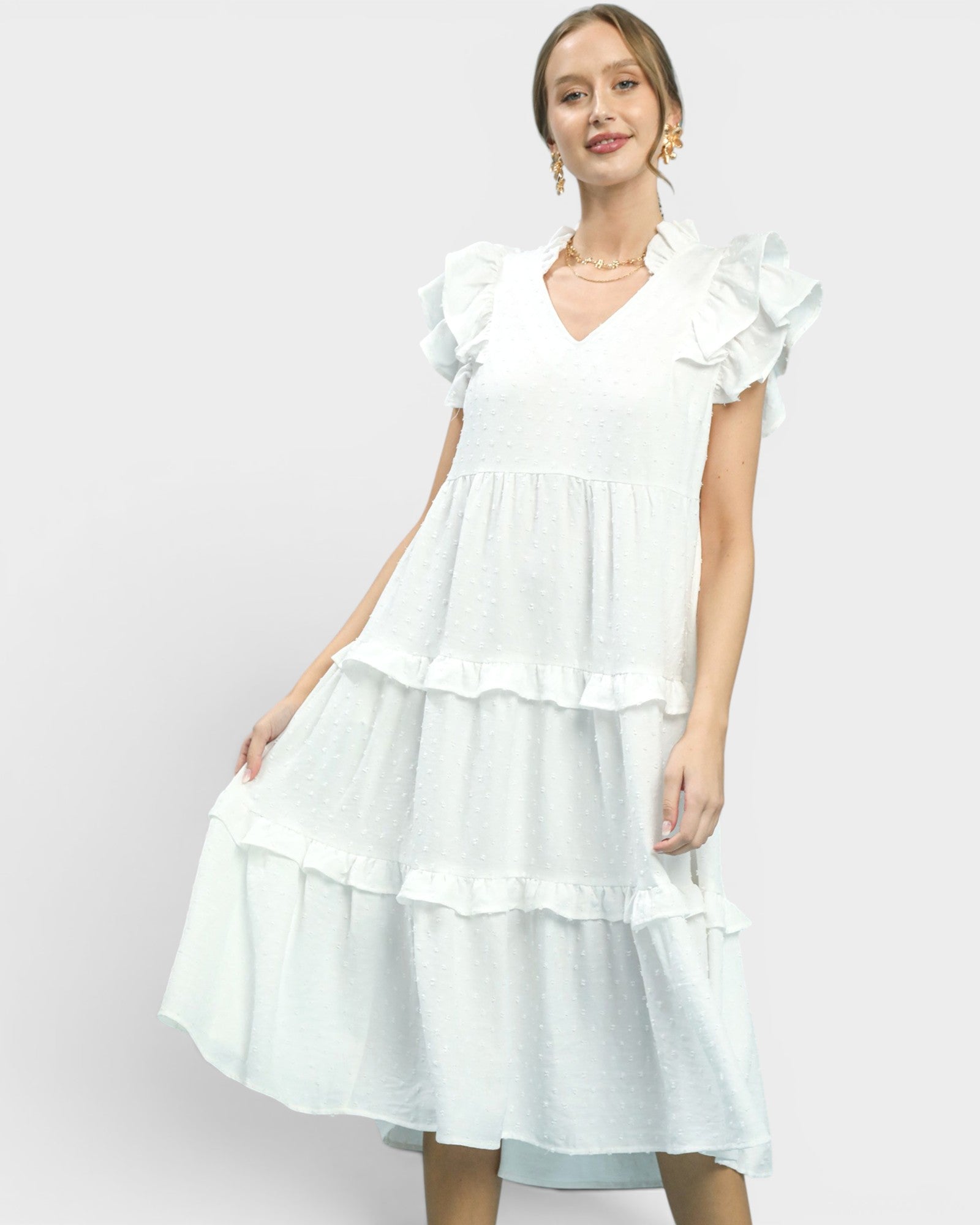 Woman wearing a white dress with ruffled sleeves and layers on a light gray background