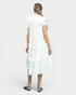 Woman wearing a white dress with ruffled sleeves and layered skirt on a plain background