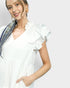 Woman wearing a white blouse with ruffled sleeves against a plain background