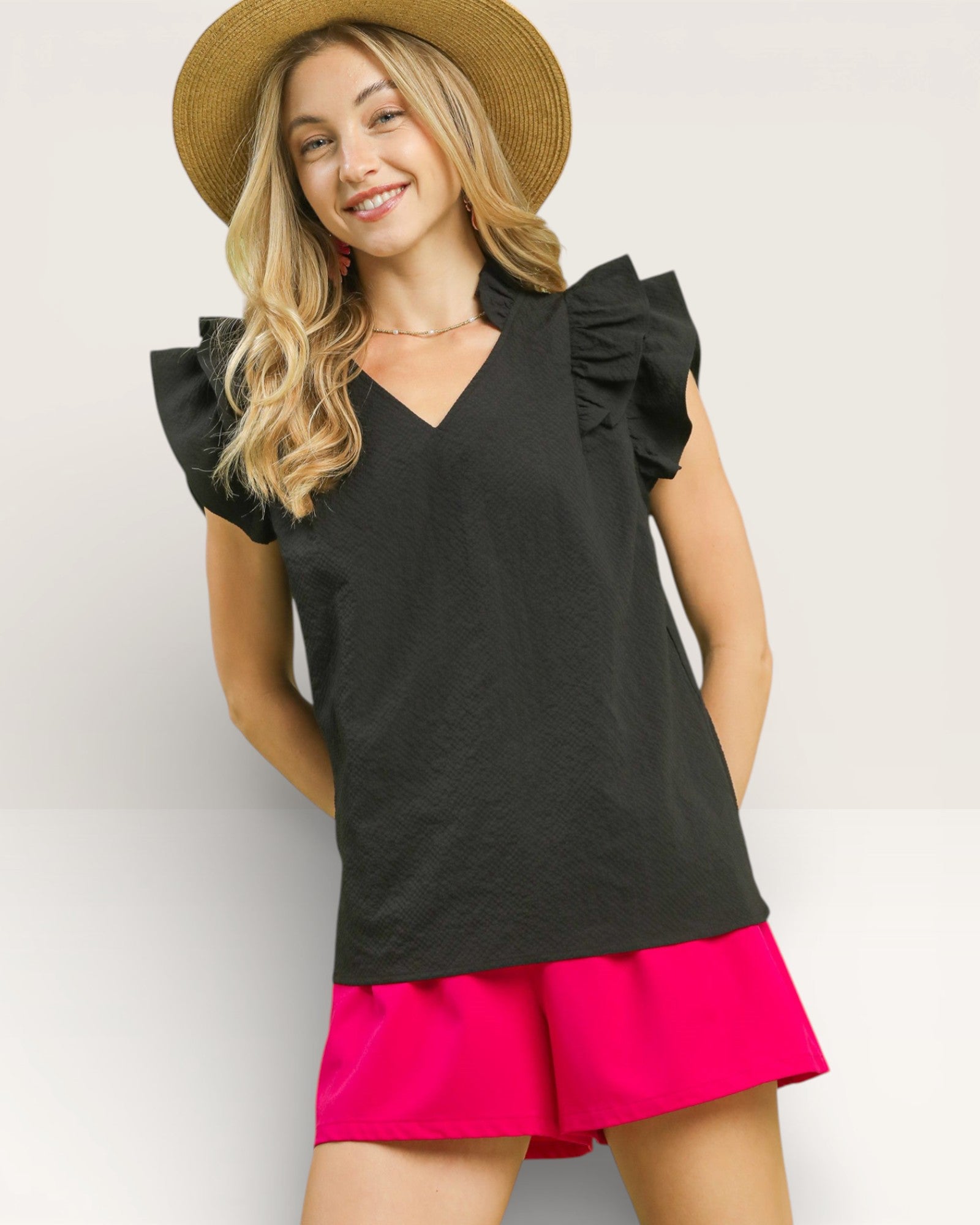 Woman wearing a black top with ruffled sleeves and a pink skirt on a white background