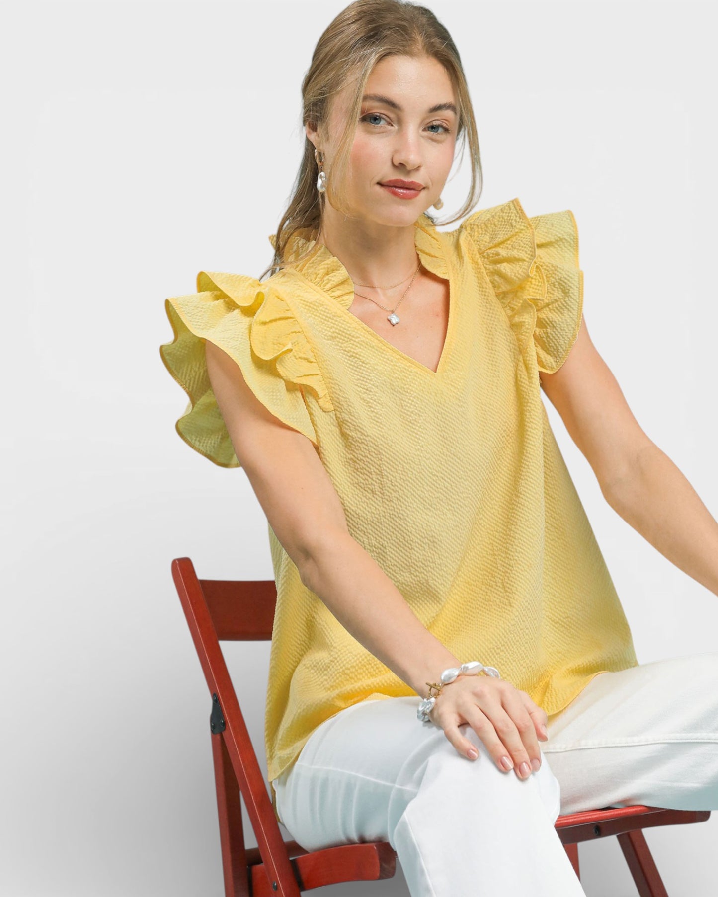 Woman wearing a yellow blouse with ruffled sleeves sitting on a red chair against a white background