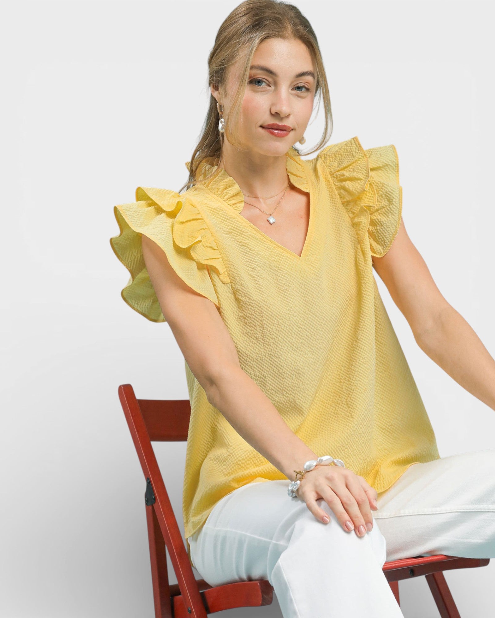 Woman wearing a yellow blouse with ruffled sleeves sitting on a red chair against a white background