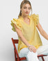Woman wearing a yellow blouse with ruffled sleeves sitting on a red chair against a white background