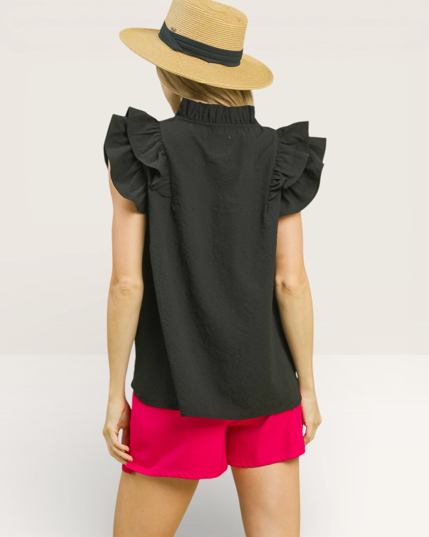 Person wearing a black sleeveless top with ruffled shoulders and pink shorts on a plain background