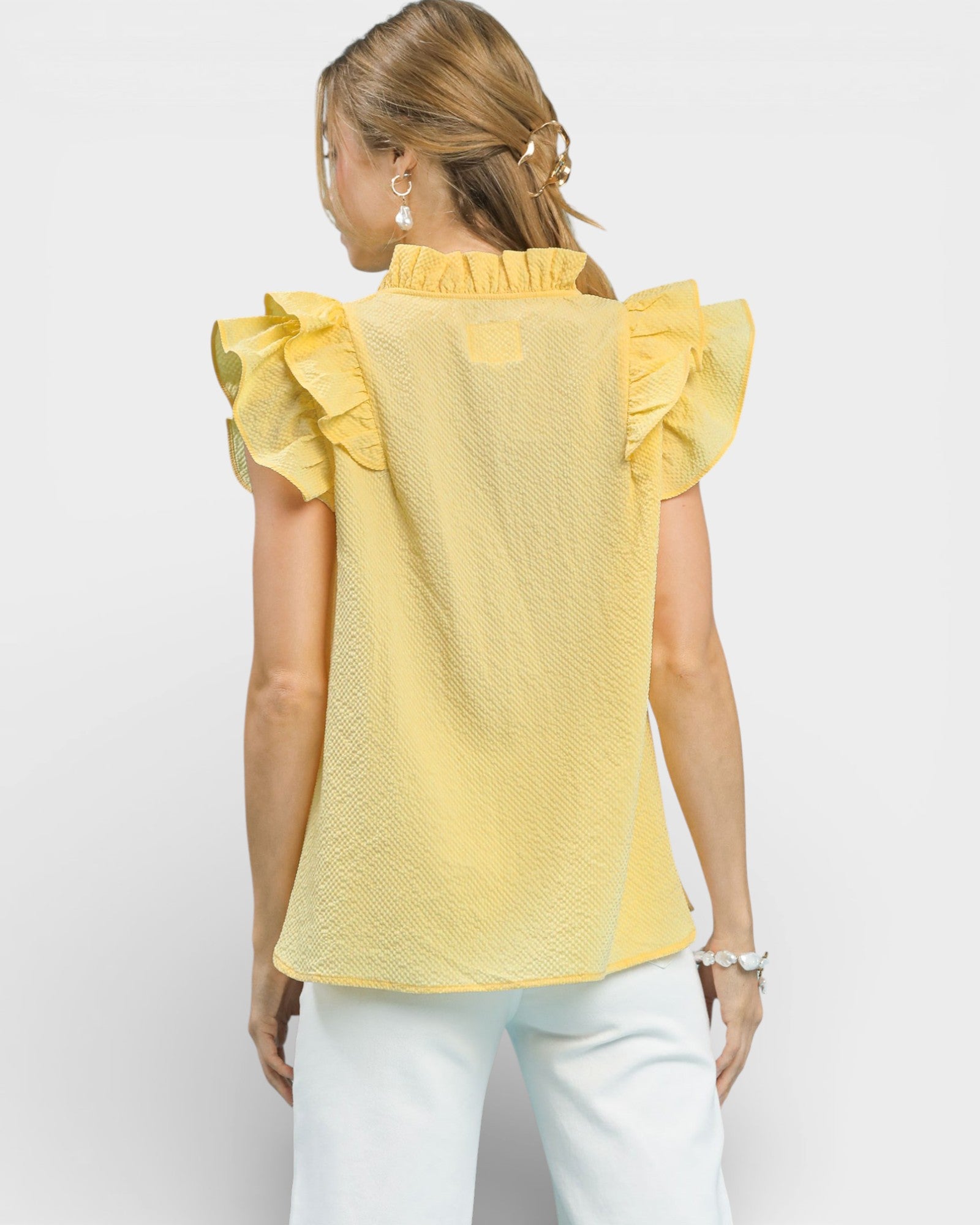 Woman wearing a yellow top with ruffled sleeves on a white background
