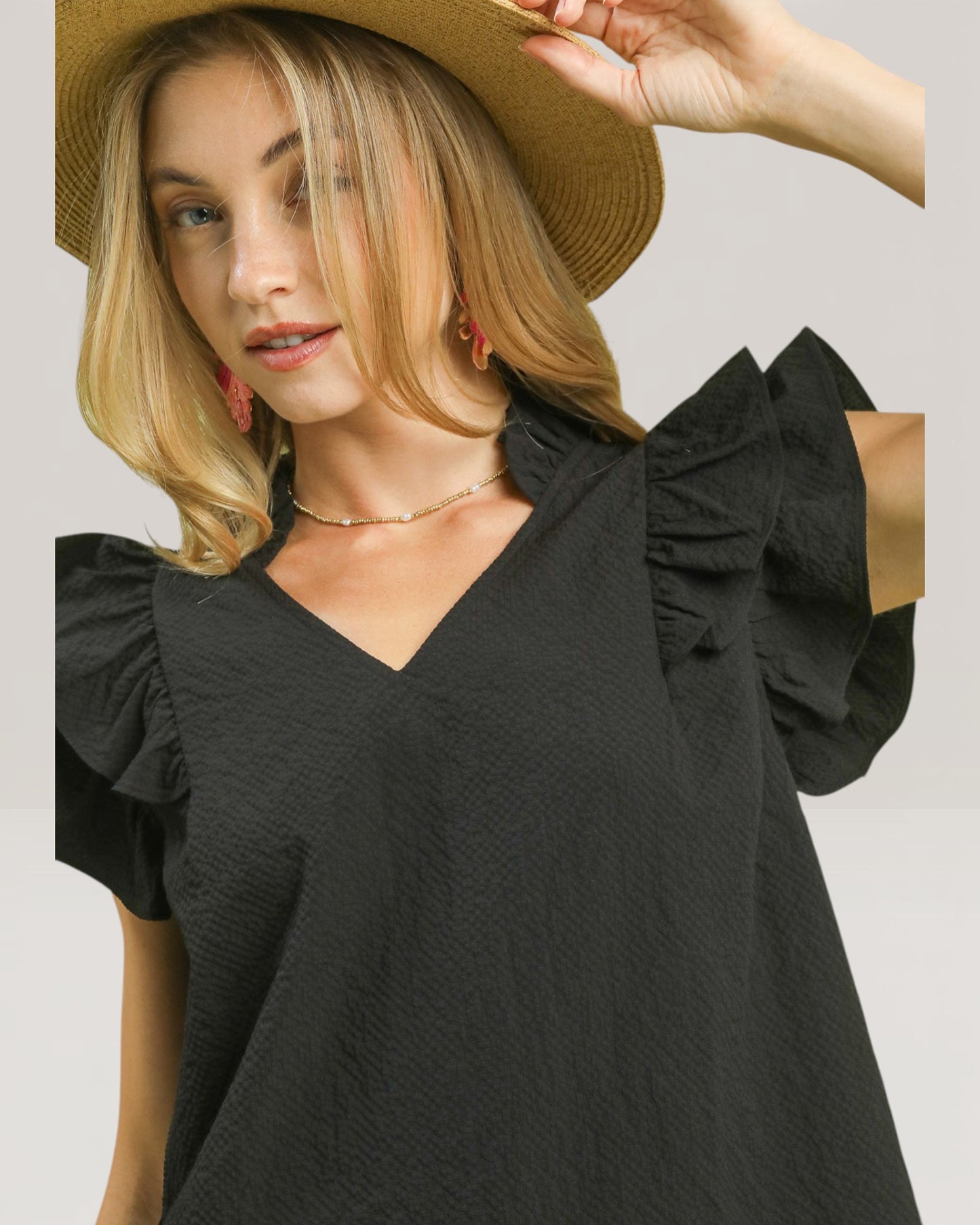 Woman wearing a black top with ruffled sleeves and a straw hat on a plain background