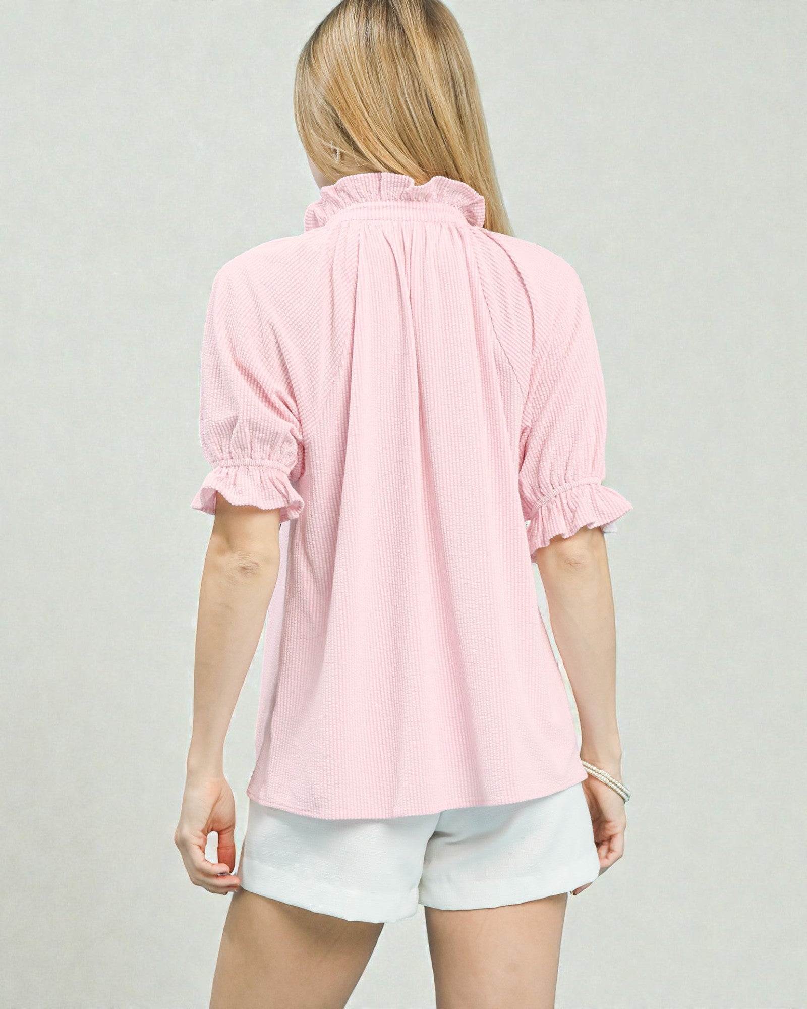 Person wearing a pink blouse and white shorts on a plain background