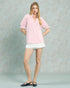 Woman wearing a pink blouse and white shorts against a plain background