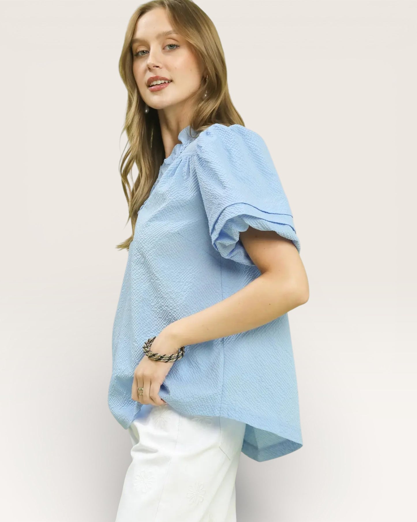 Woman wearing a light blue top with ruffled sleeves against a plain background