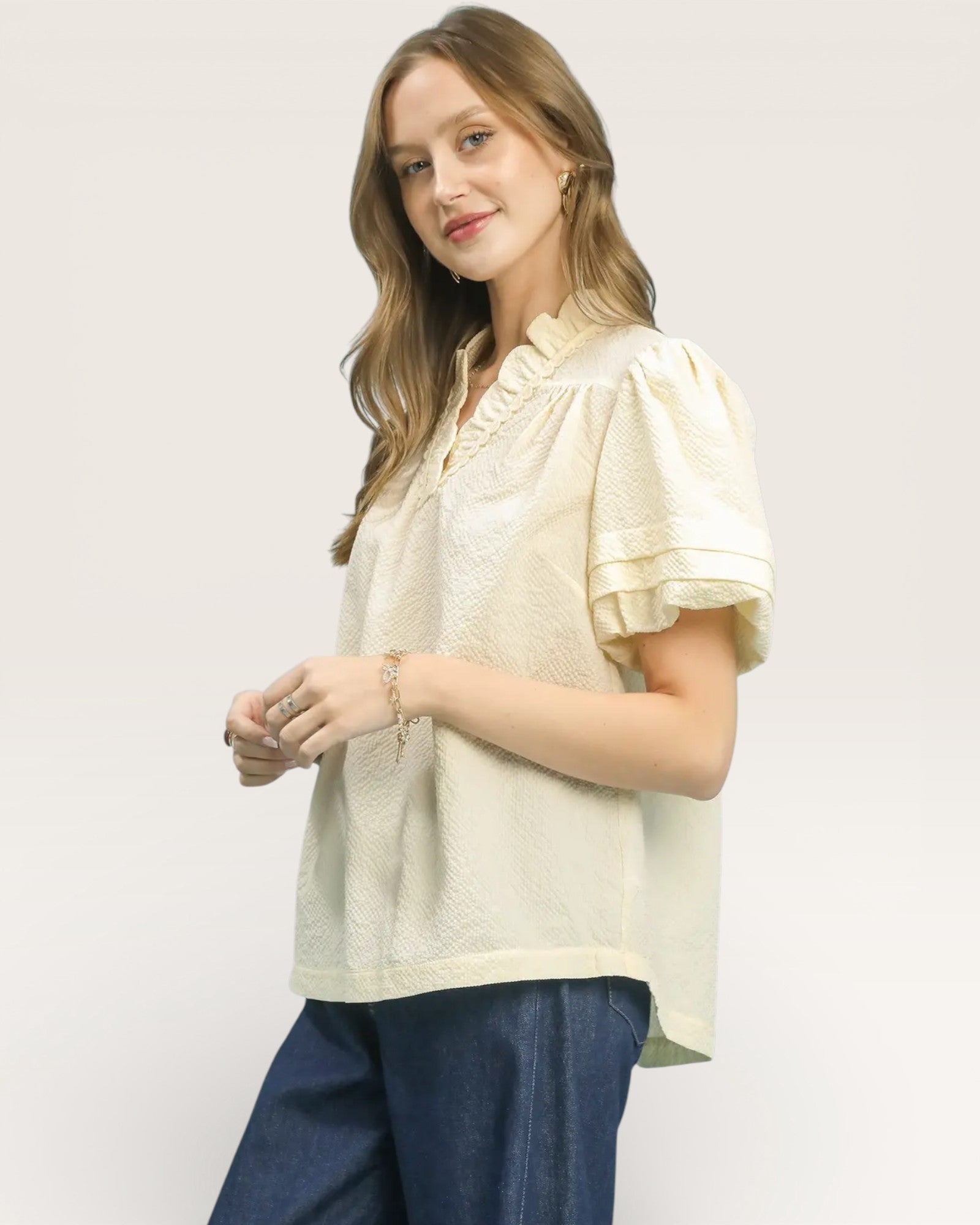 Woman wearing a light-colored blouse with short sleeves and a collar, standing against a plain background.