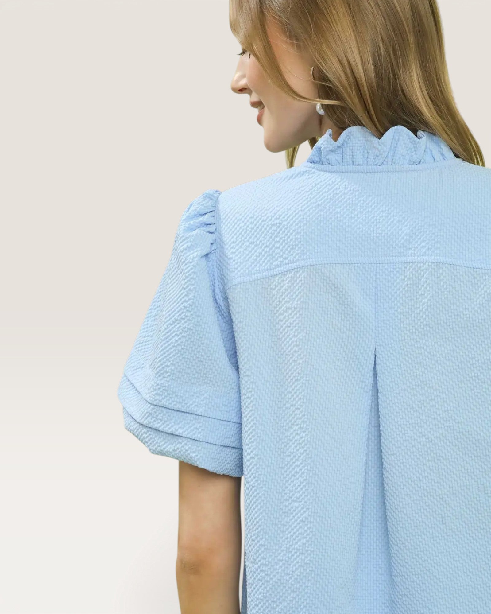 Woman wearing a light blue textured blouse against a plain background