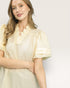 Woman wearing a light yellow dress with ruffled details on a plain background
