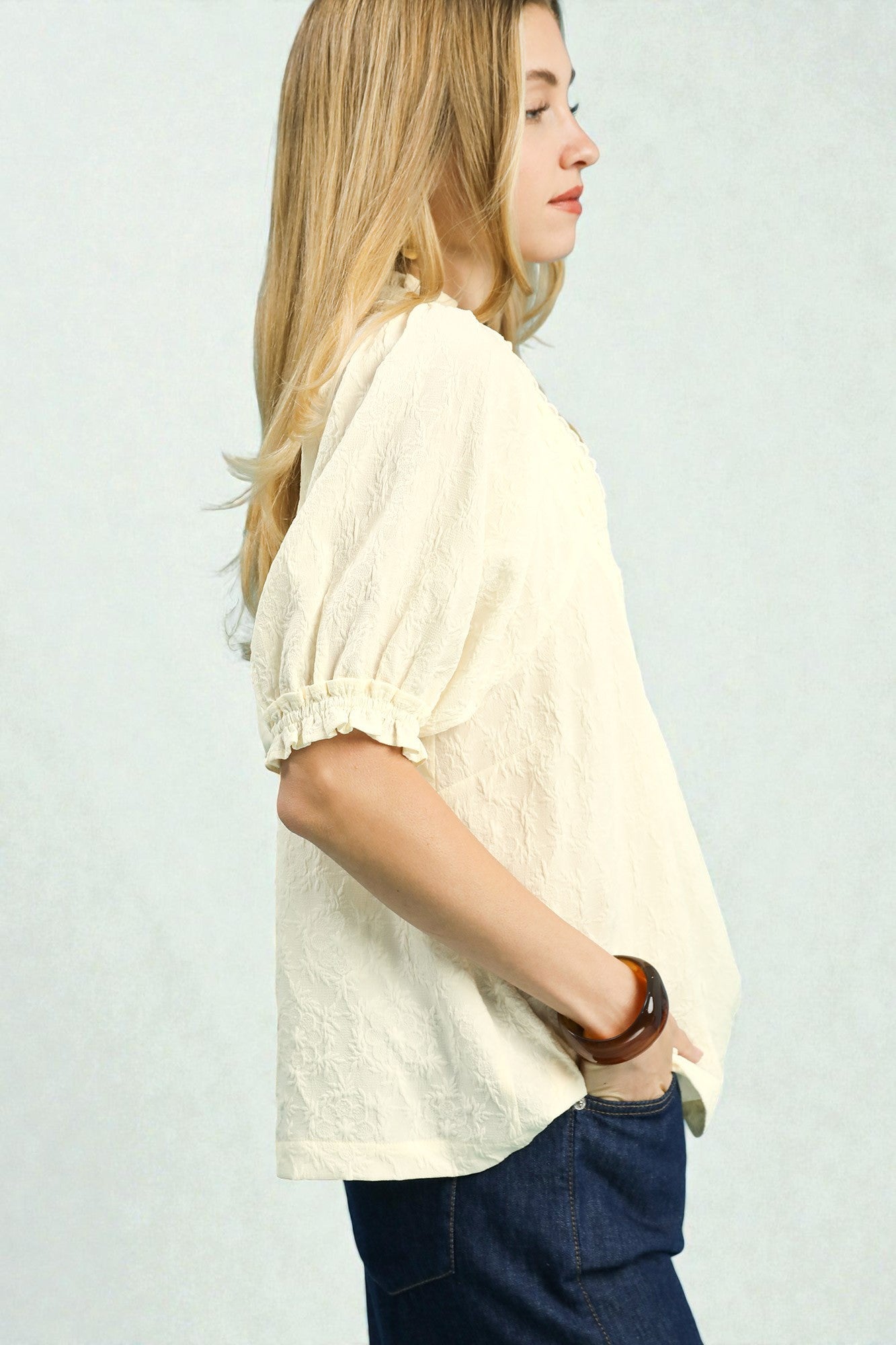 Woman wearing a light-colored blouse and dark pants against a plain background