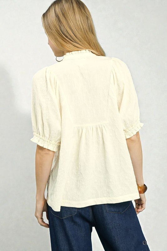 Person wearing a light-colored blouse and dark pants on a plain background