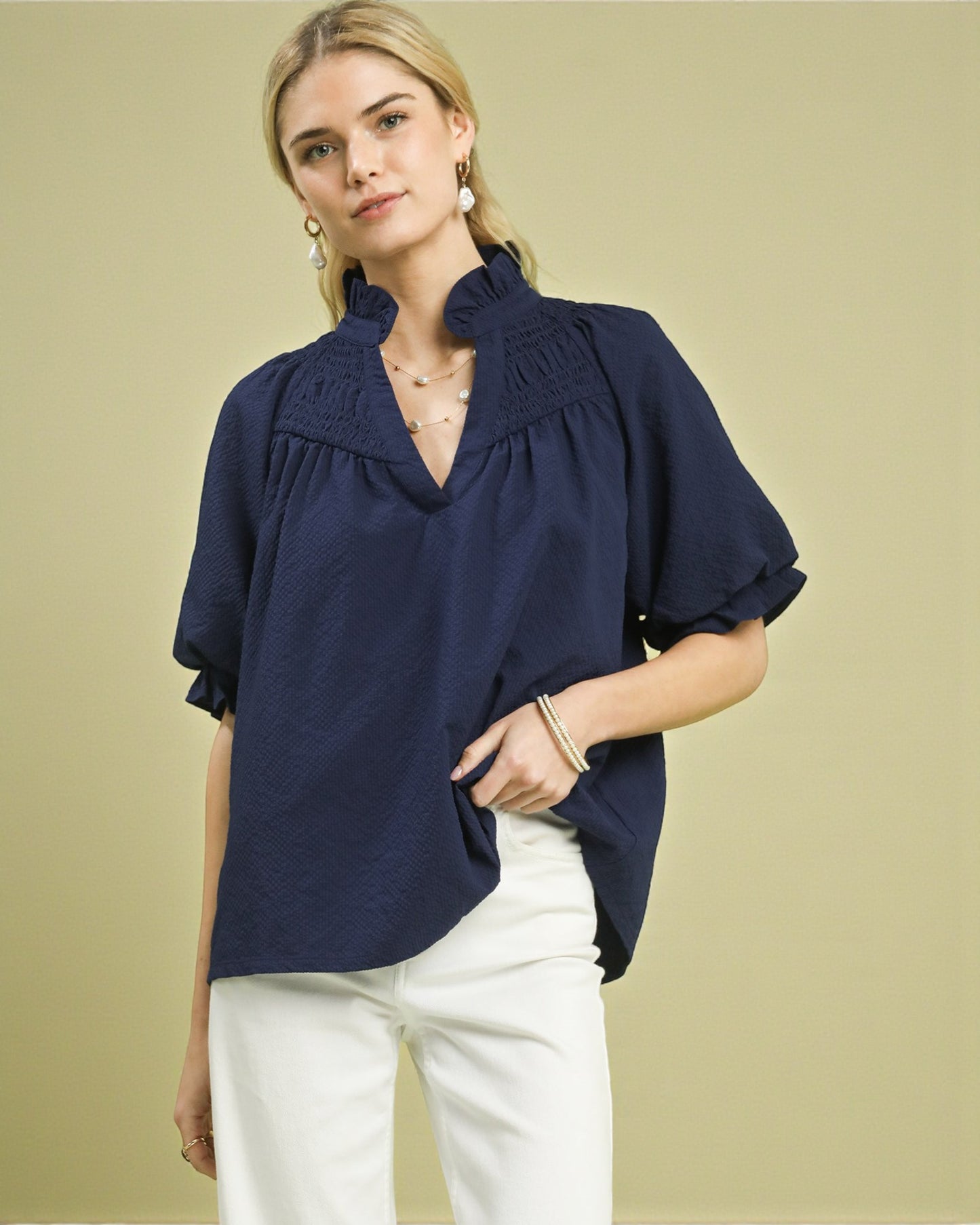 Woman wearing a navy blue blouse with ruffled details on a beige background