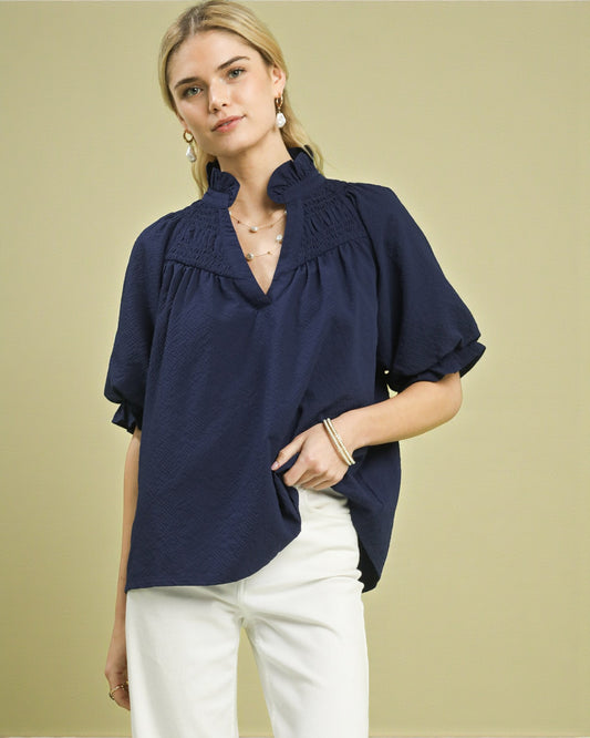 Woman wearing a navy blue blouse with ruffled details on a beige background