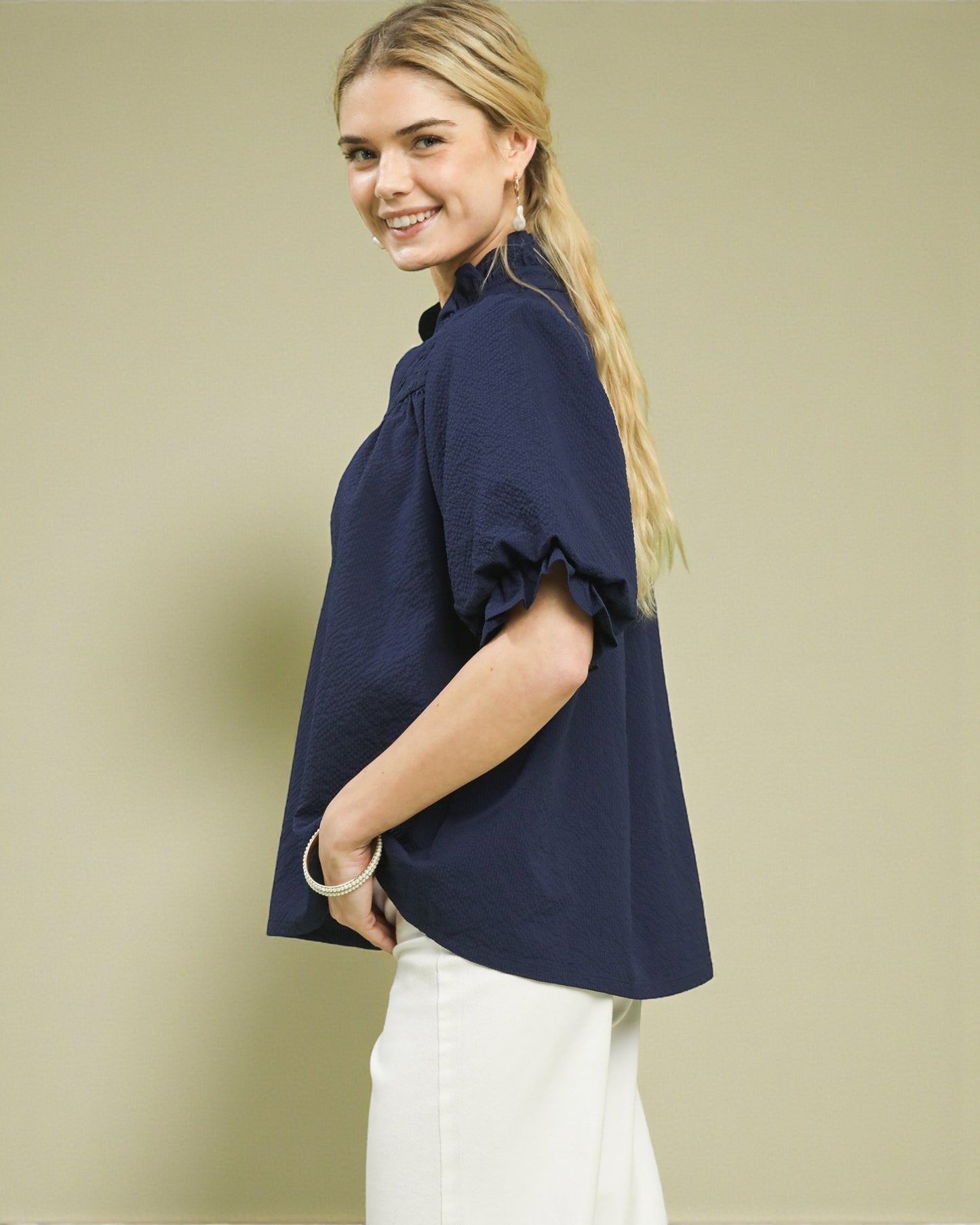Woman wearing a navy blue blouse with white pants against a beige background