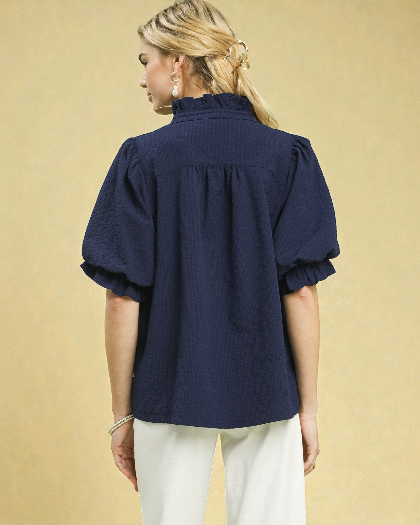 Woman wearing a navy blue blouse with puff sleeves on a beige background