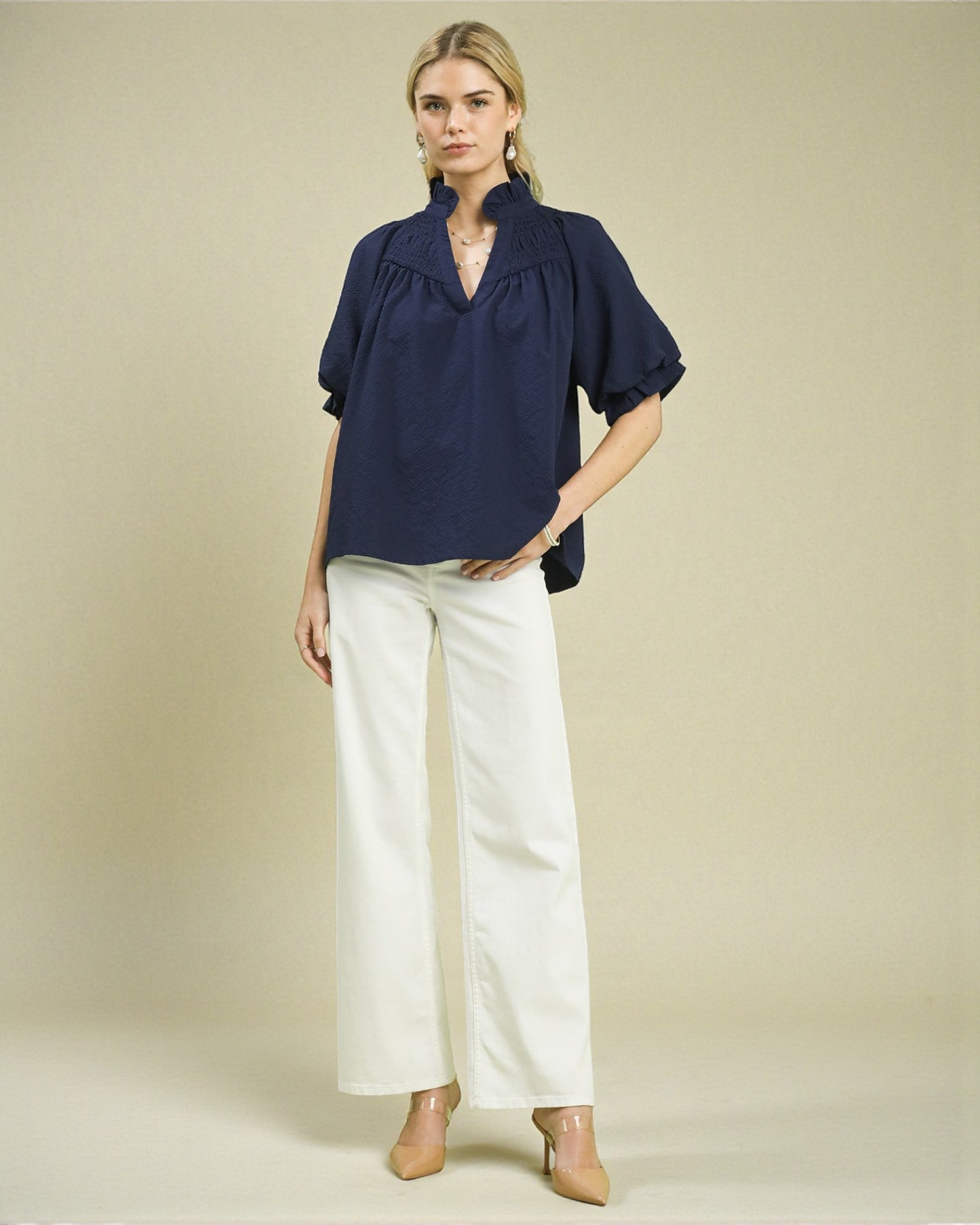 Woman wearing a navy blouse and white pants on a beige background
