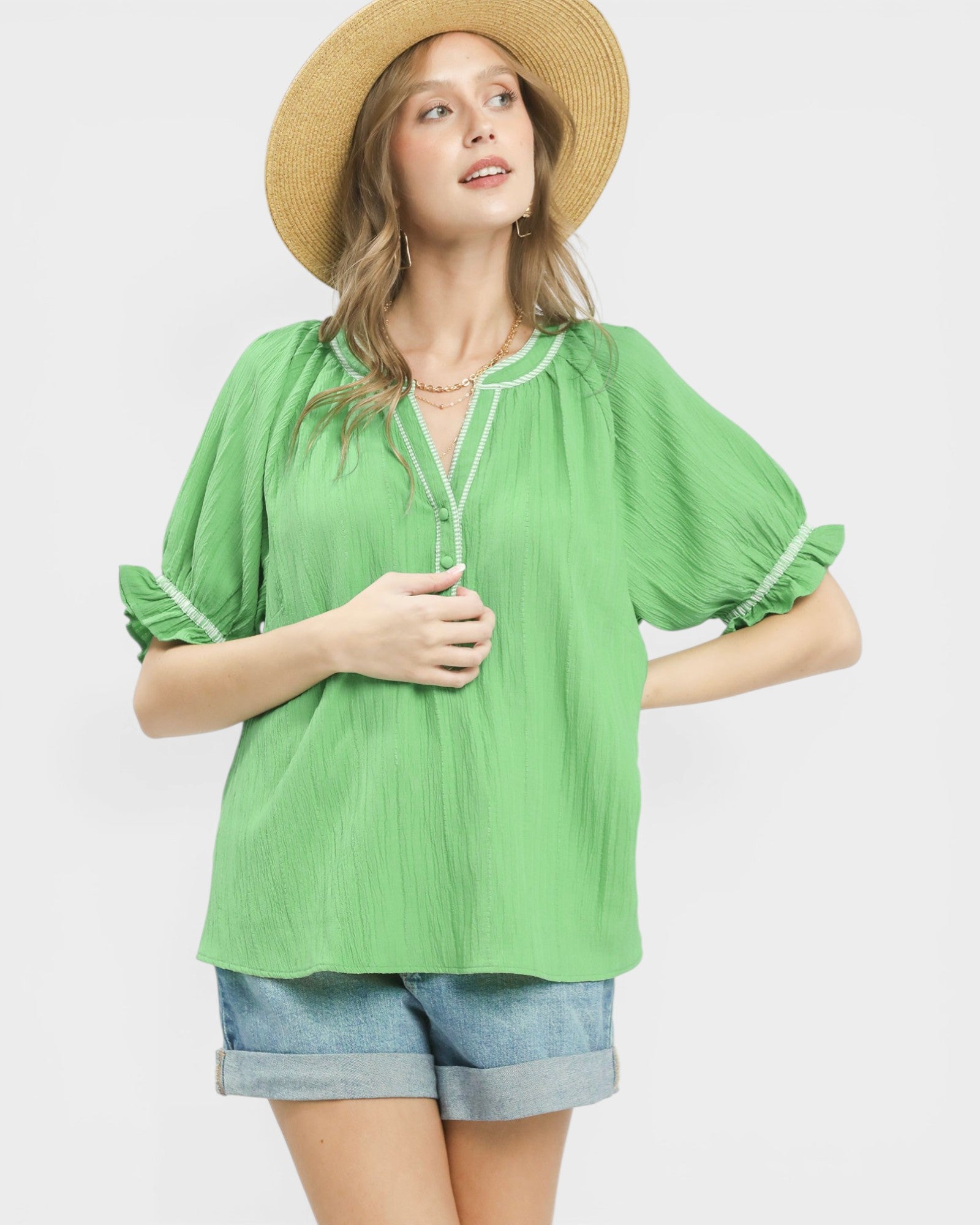 Woman wearing a green blouse, denim shorts, and a straw hat on a white background