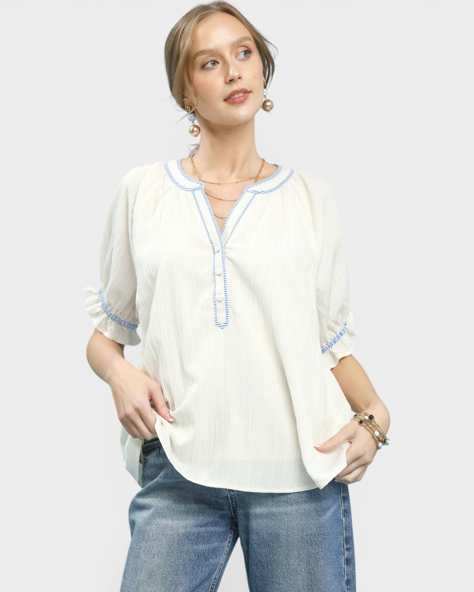 Woman wearing a white blouse with blue trim and blue jeans on a light gray background