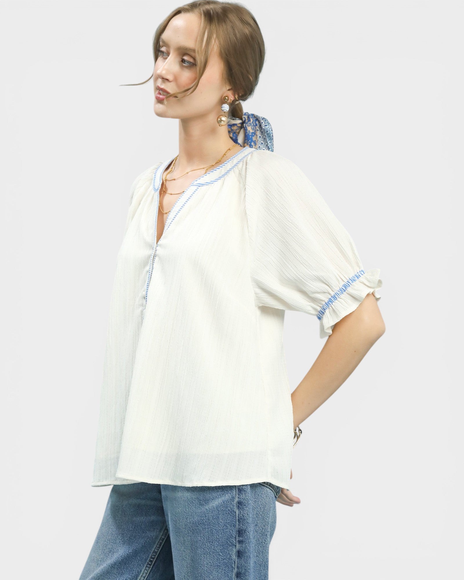 Woman wearing a white blouse with blue accents and blue jeans on a plain background