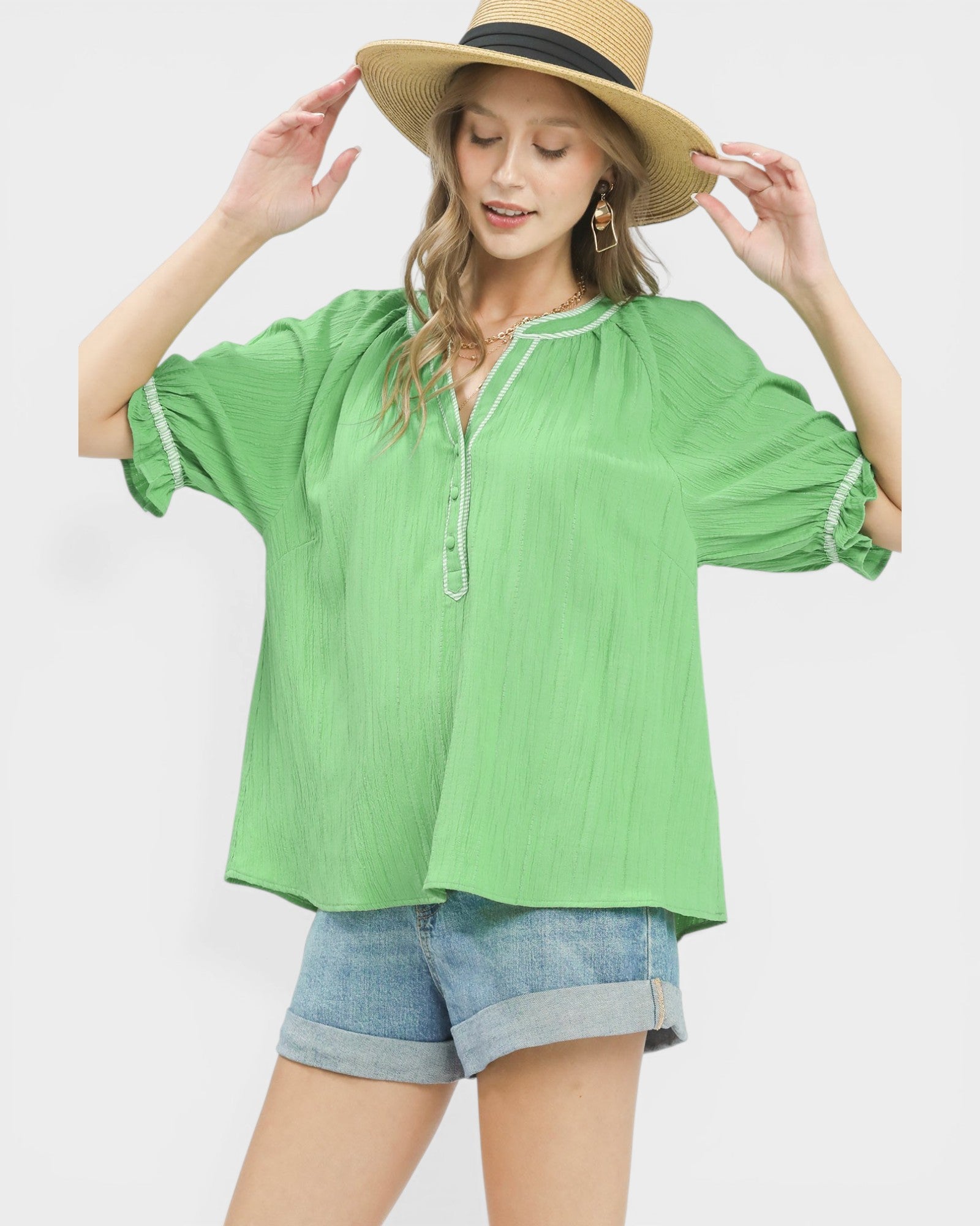 Woman wearing a green blouse and denim shorts with a straw hat on a white background