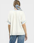 Woman wearing a white blouse with blue accents and blue jeans on a light gray background