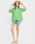 Woman wearing a green top and denim shorts with a straw hat on a white background