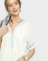 Woman wearing a white outfit with blue accents against a plain background