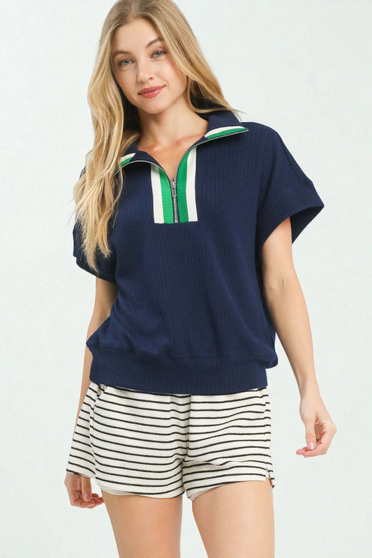 Woman wearing a navy blue top with a green and white stripe and striped shorts on a white background