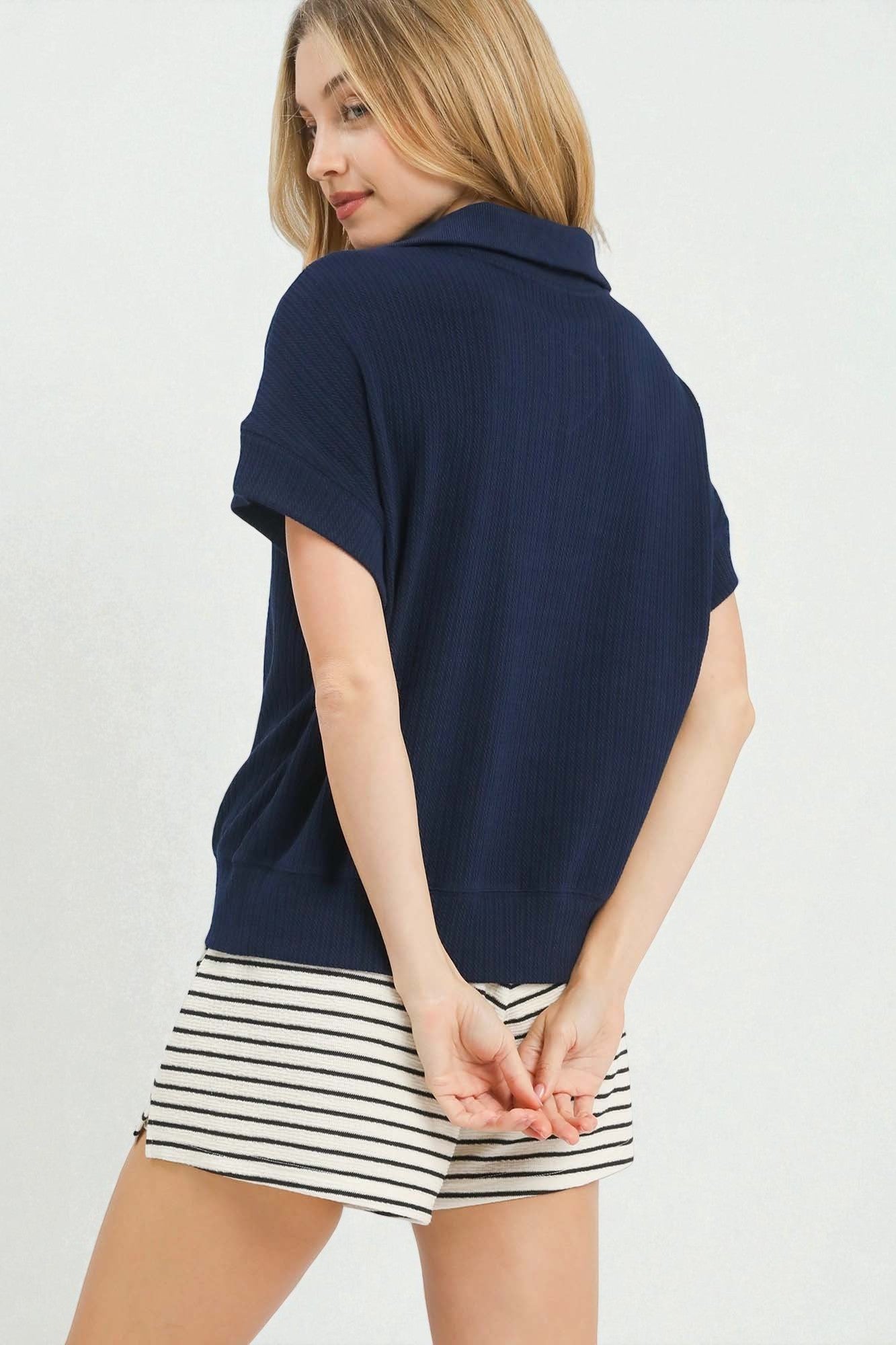Woman wearing a navy blue top and striped shorts on a plain background