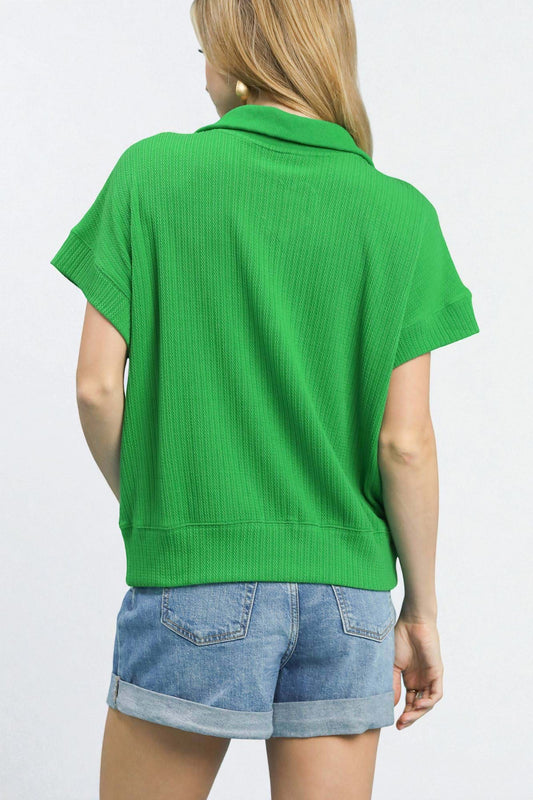 Green short-sleeve top worn by a person on a white background