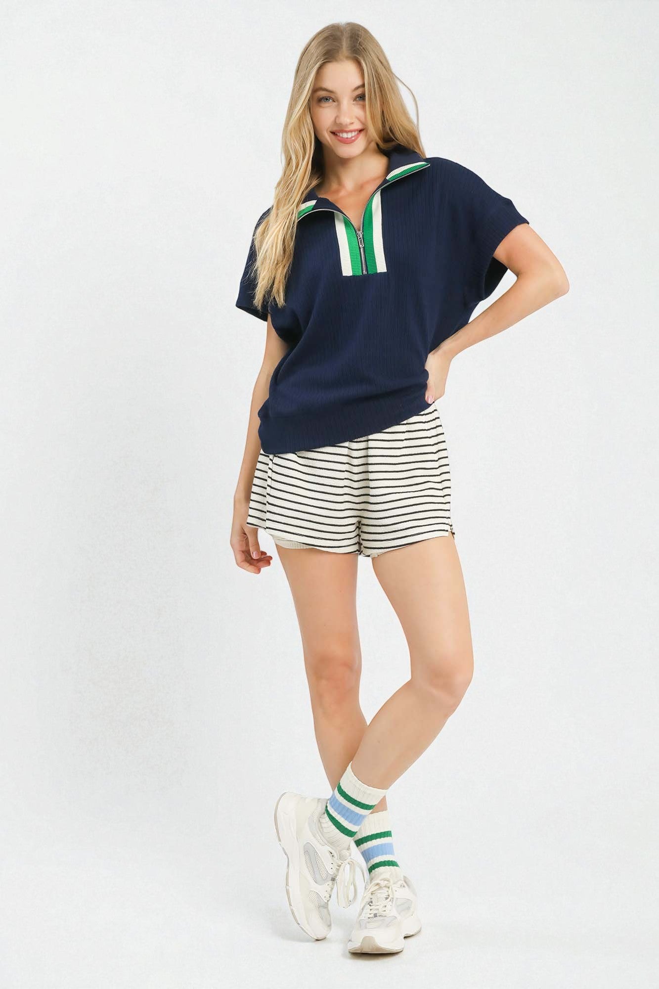 Woman wearing a navy blue top with a green stripe and striped shorts on a white background