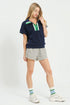 Woman wearing a navy polo shirt with green accents and striped shorts on a white background
