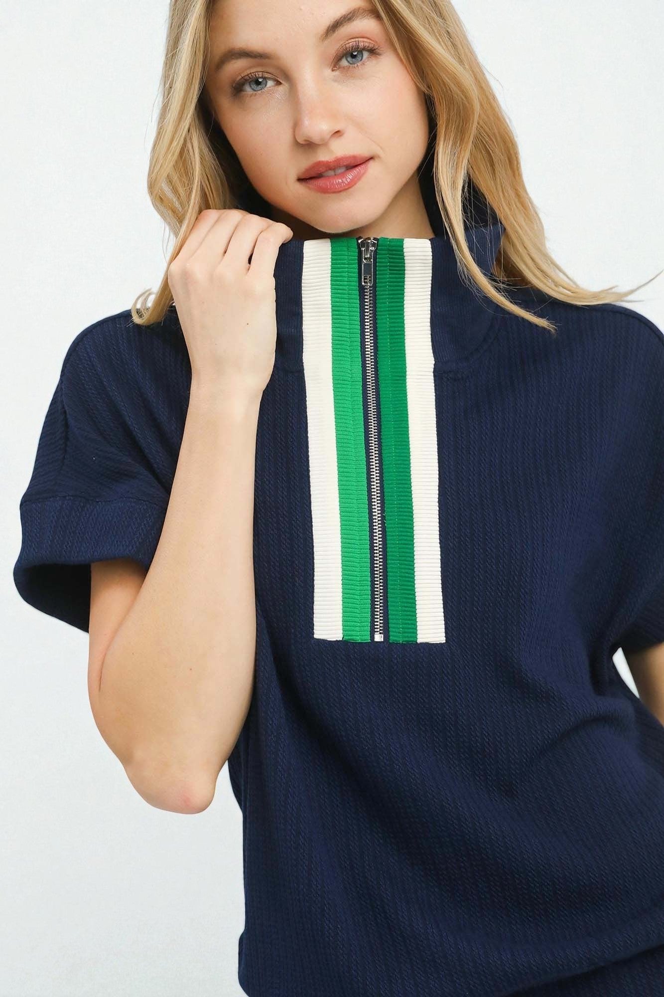 Woman wearing a navy sweater with a green and white stripe and zipper on a white background