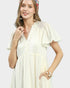 Woman wearing a light yellow dress with ruffled sleeves on a plain background